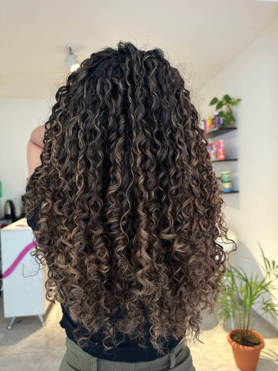 Mujer de espaldas mostrando su cabello rizado largo, con algunas iluminaciones rubias