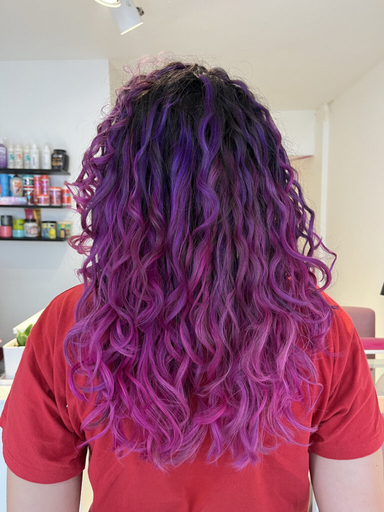 Mujer de espaldas mostrando combinación de fucsia y violeta fantasía en una base de cabello oscura